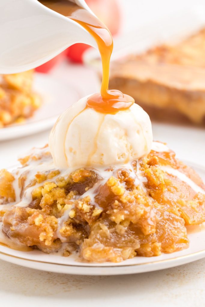 Easy caramel apple dump cake on a plate with a scoop of vanilla ice cream on top and caramel sauce being poured over the ice cream. 