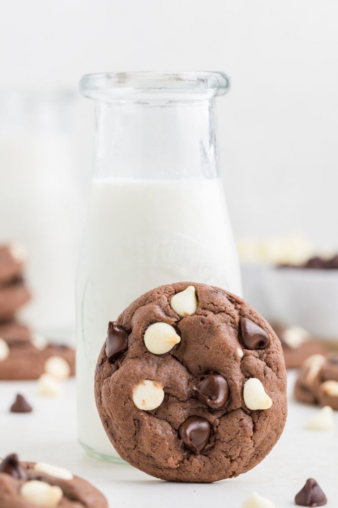 Triple chocolate cake mix cookie propped against a bottle of milk. 