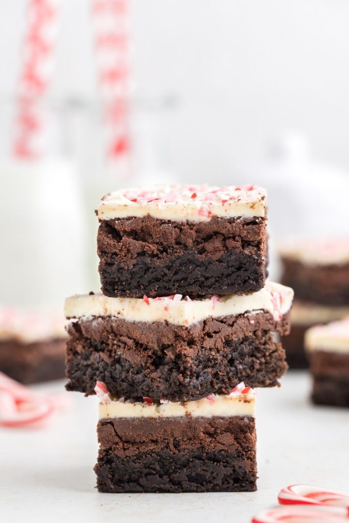 Three peppermint bark brownies stacked on each other with two glasses of milk in the background. 