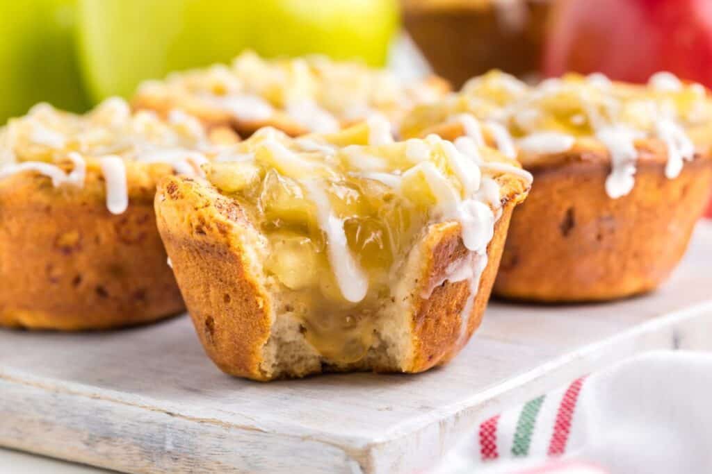 Close-up of apple pie cinnamon rolls muffins topped with icing, on a wooden board.