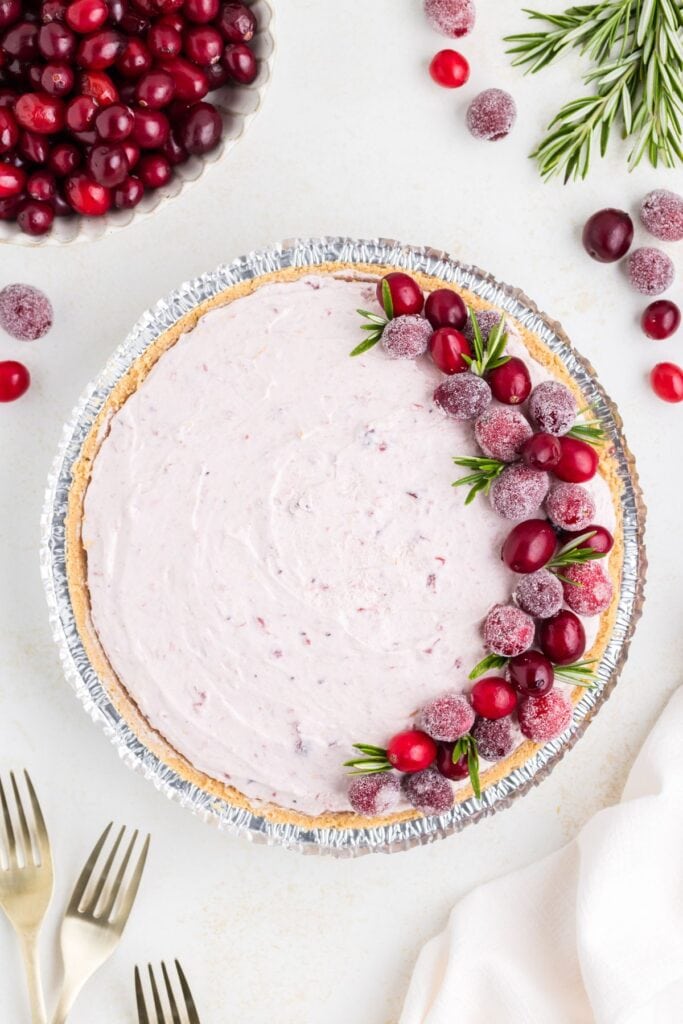 No-bake cranberry pie with sugared cranberries and rosemary in foil pan, gold forks and cranberries beside.