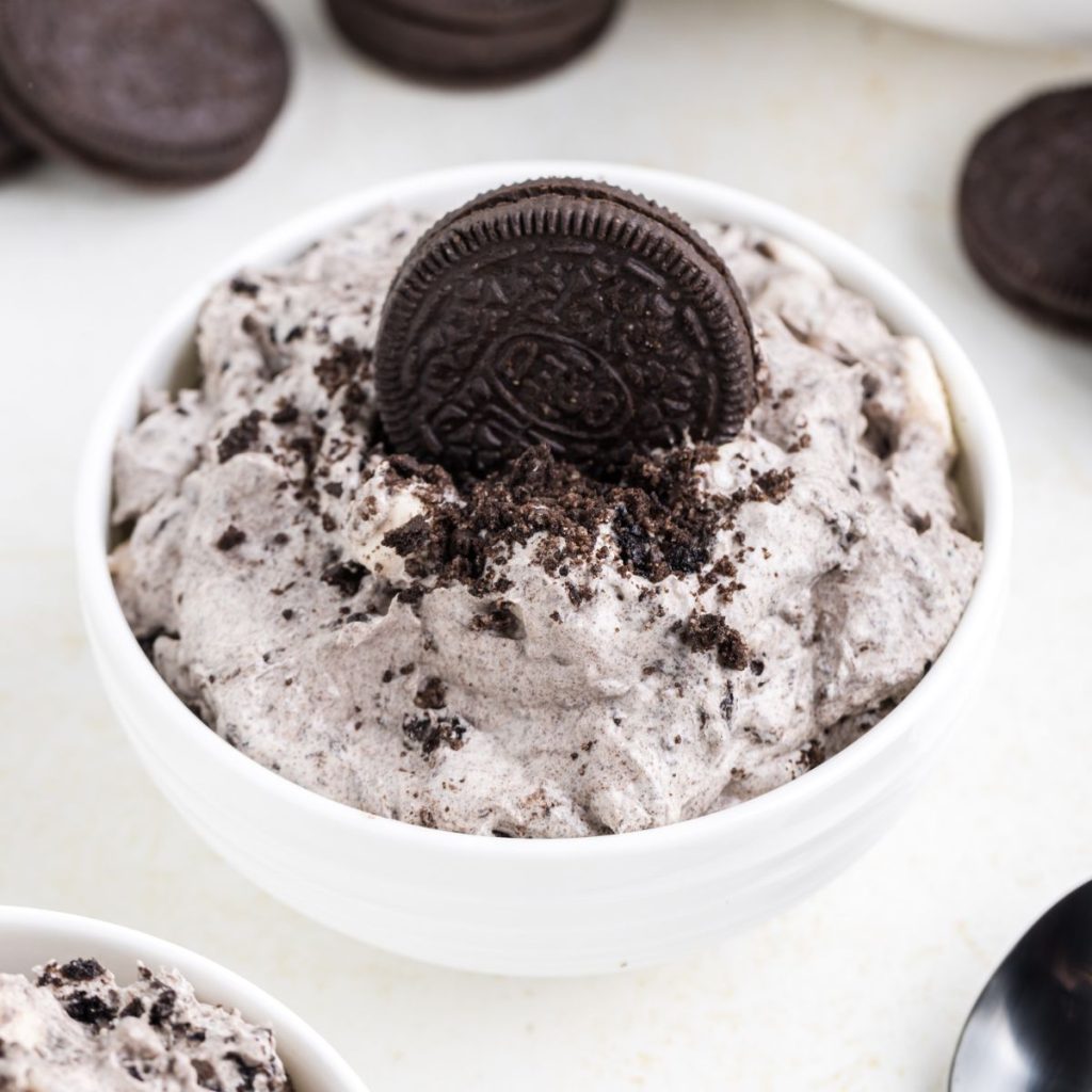 A bowl of Oreo fluff dessert topped with crushed oreos and a whole cookie