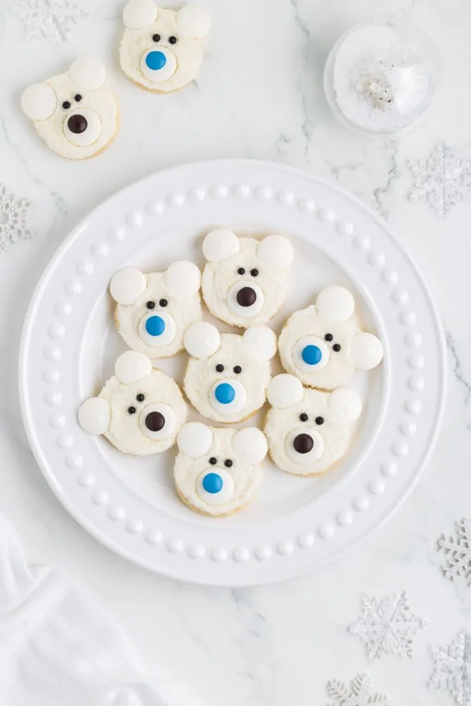 Seven polar face cookies displayed on a round white plate surrounded by snowflake decorations