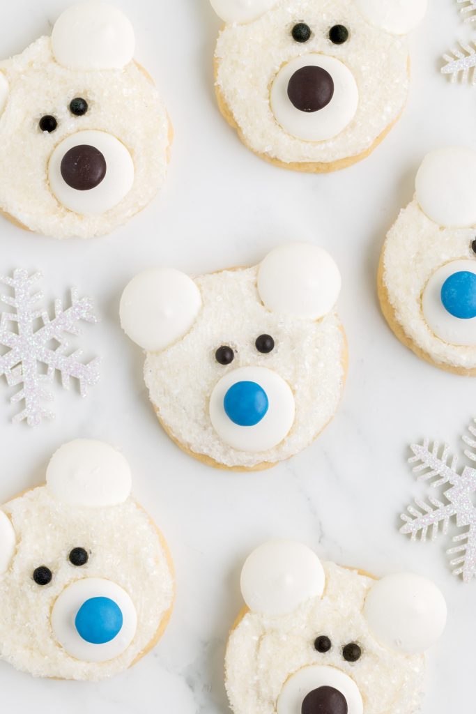 Six polar bear face cookies spread out on the counter with snow flake decorations.