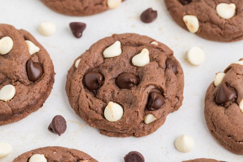 Close-up of triple chocolate cookies with white and dark chocolate chips on a light-colored surface.
