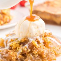 Easy caramel apple dump cake on a plate with a scoop of vanilla ice cream on top and caramel sauce being poured over the ice cream.