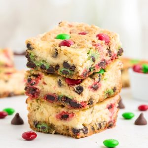 Three Christmas Cookie Cheesecake Bars stacked on the counter with two milk bottles in the background.