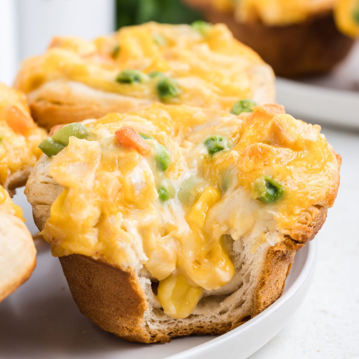 Close-up of a baked mini chicken pot pie filled with melted cheese, chunks of vegetables, and creamy filling on a white plate.