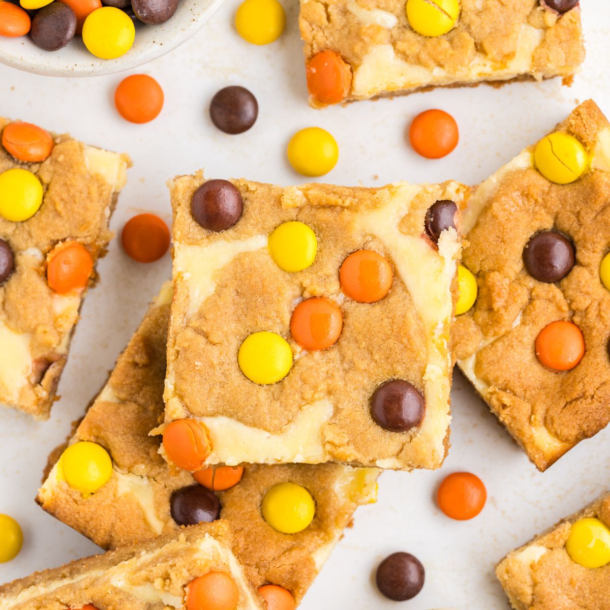 Stack of Peanut Butter Cookie Cheesecake Bars surrounded by Reese's Pieces.