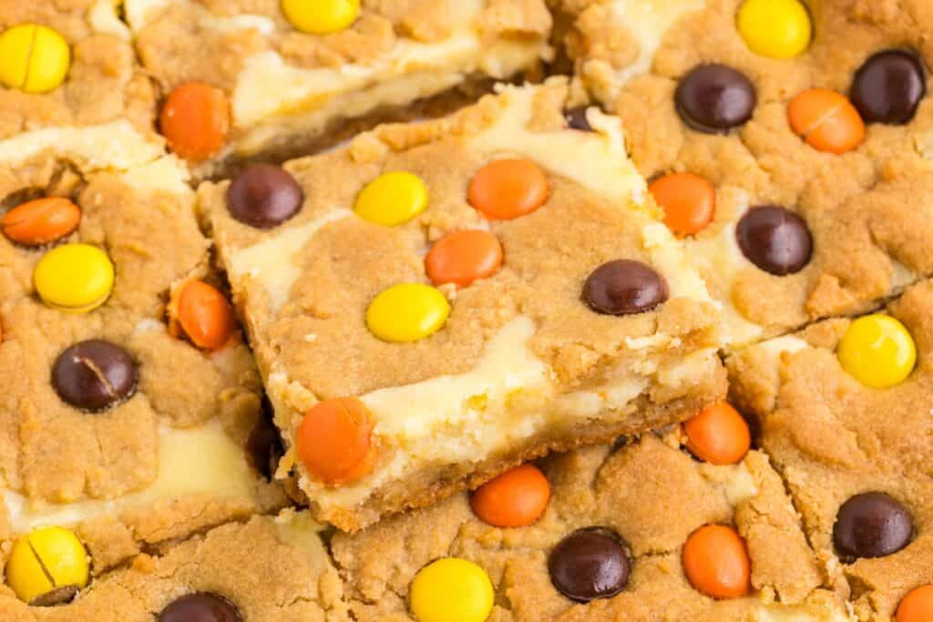 Close-up of peanut butter cookie cheesecake bars topped with orange, yellow, and brown candy-coated chocolates.