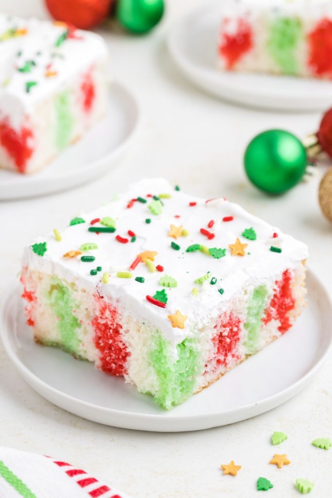 Slice of Christmas Poke Cake with red and green jello on a plate. 