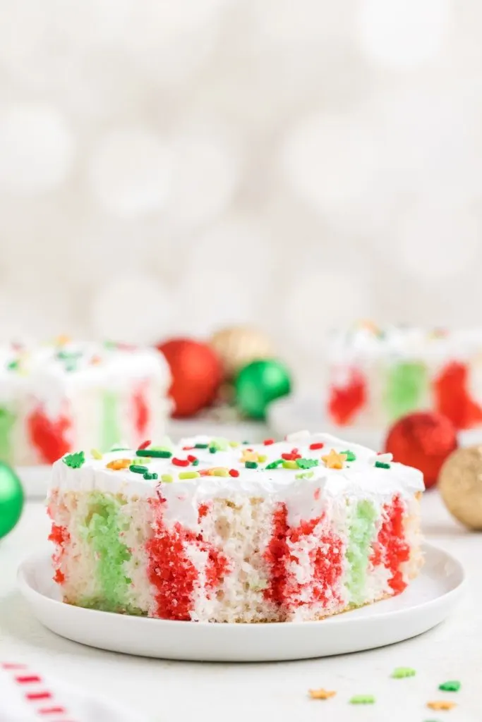 Slice of Christmas Poke Cake with red and green jello on a plate with a forkful missing. 