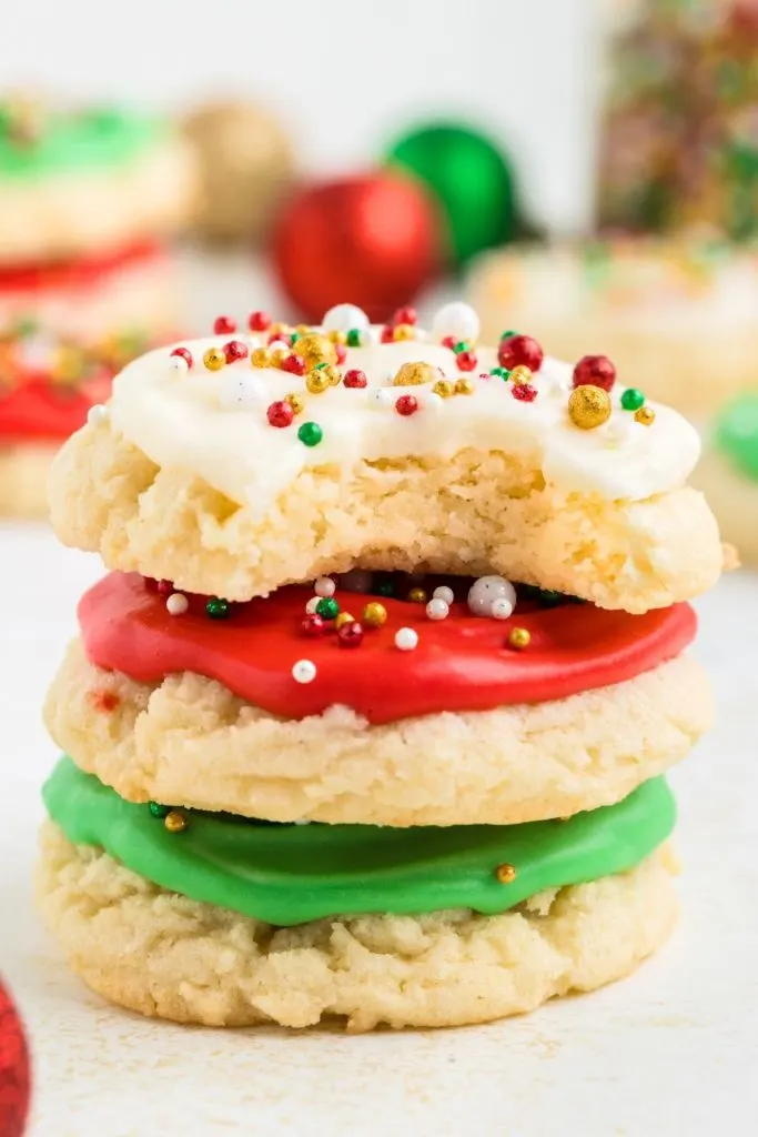 Pile of three cream cheese sugar cookies with a bite missing from the top cookie. 