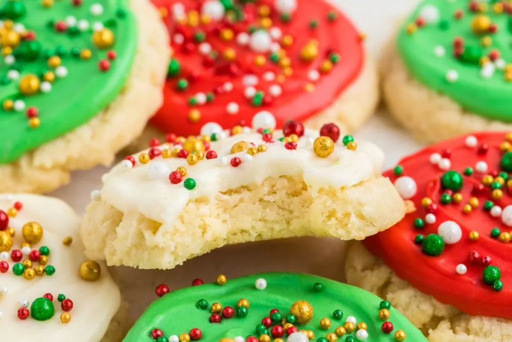 Pile of frosted sugar cookies with a bite missing from one cookie. 