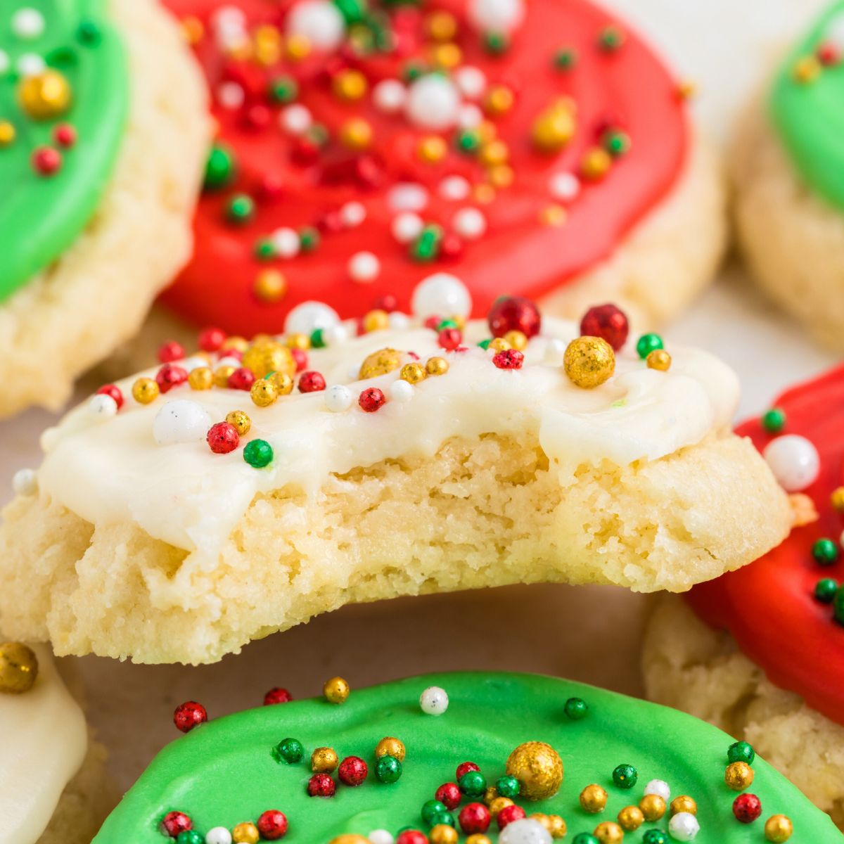 Pile of frosted sugar cookies with a bite missing from one cookie.