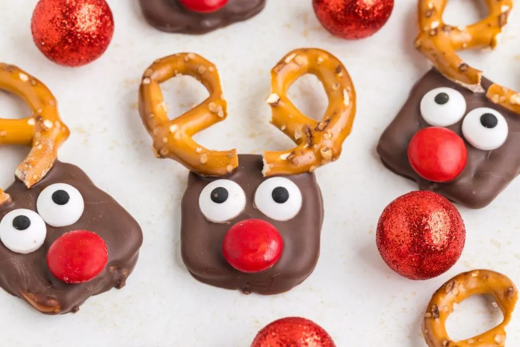 Reindeer pretzels displayed on counter surrounded by holiday ornaments.