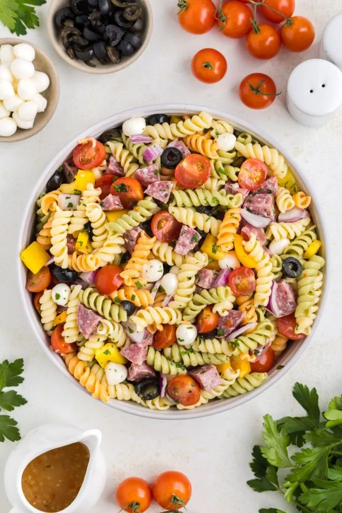 Bowl of easy Italian pasta salad on the counter surrounded by ingredients. 