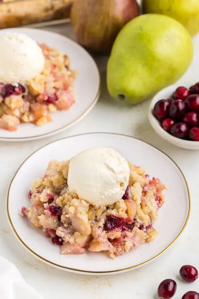 Two plates of Cranberry Pear Sugar Cookie Crumble topped with vanilla ice cream. 