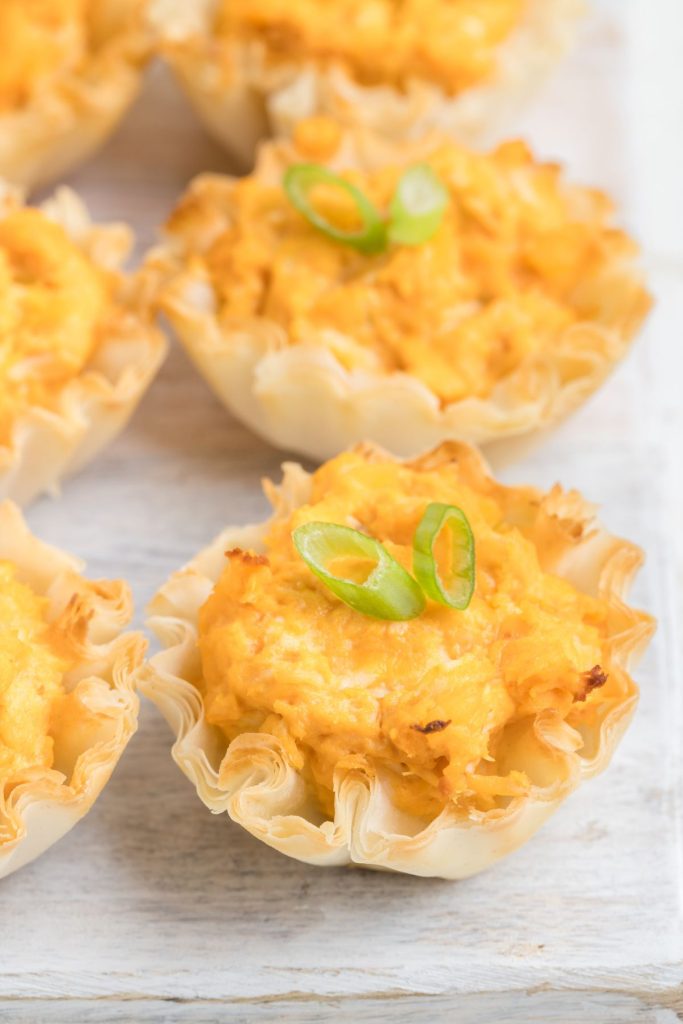 Buffalo chicken phyllo cups arranged in rows on a wooden board. 