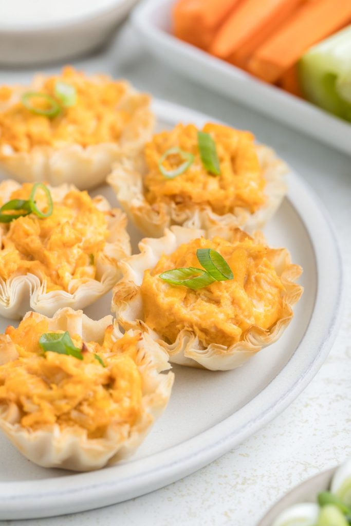 Buffalo chicken phyllo cups on a plate with carrots and celery in the background. 