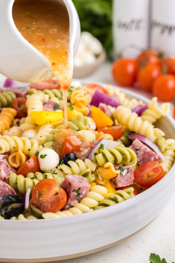 Italian dressing being poured over bowl of pasta salad.
