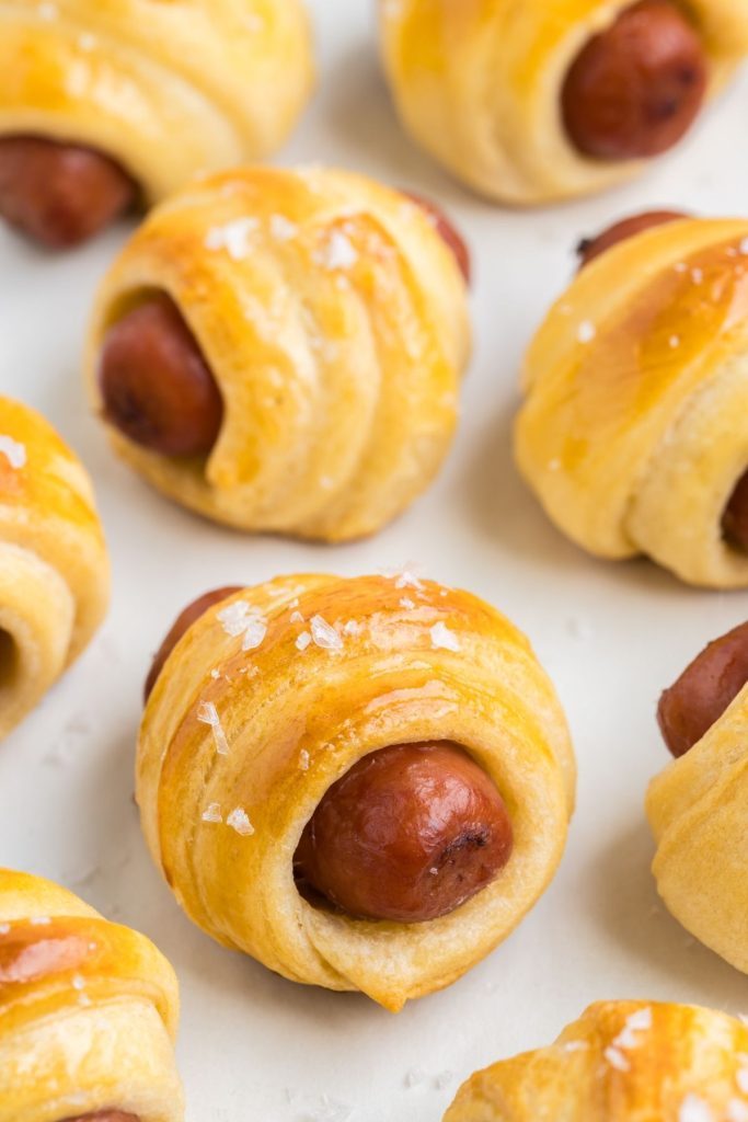 Crescent roll pigs in a blanket arranged on a parchment lined tray. 