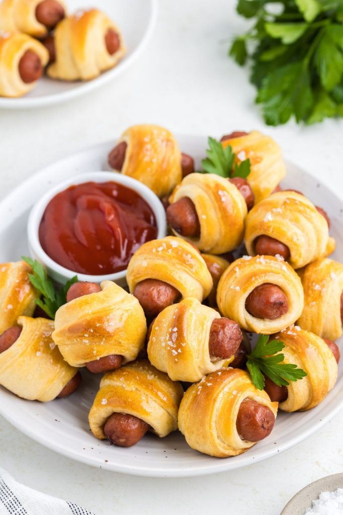 Pigs in a blanket made with crescent rolls piled on a plate with a small bowl of ketchup.