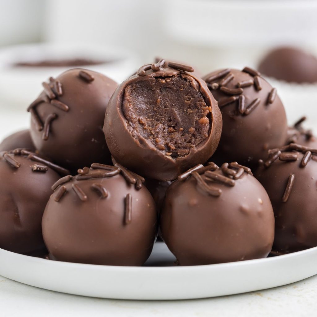 Brownie truffles piled on a plate with a bite missing from the top truffle.