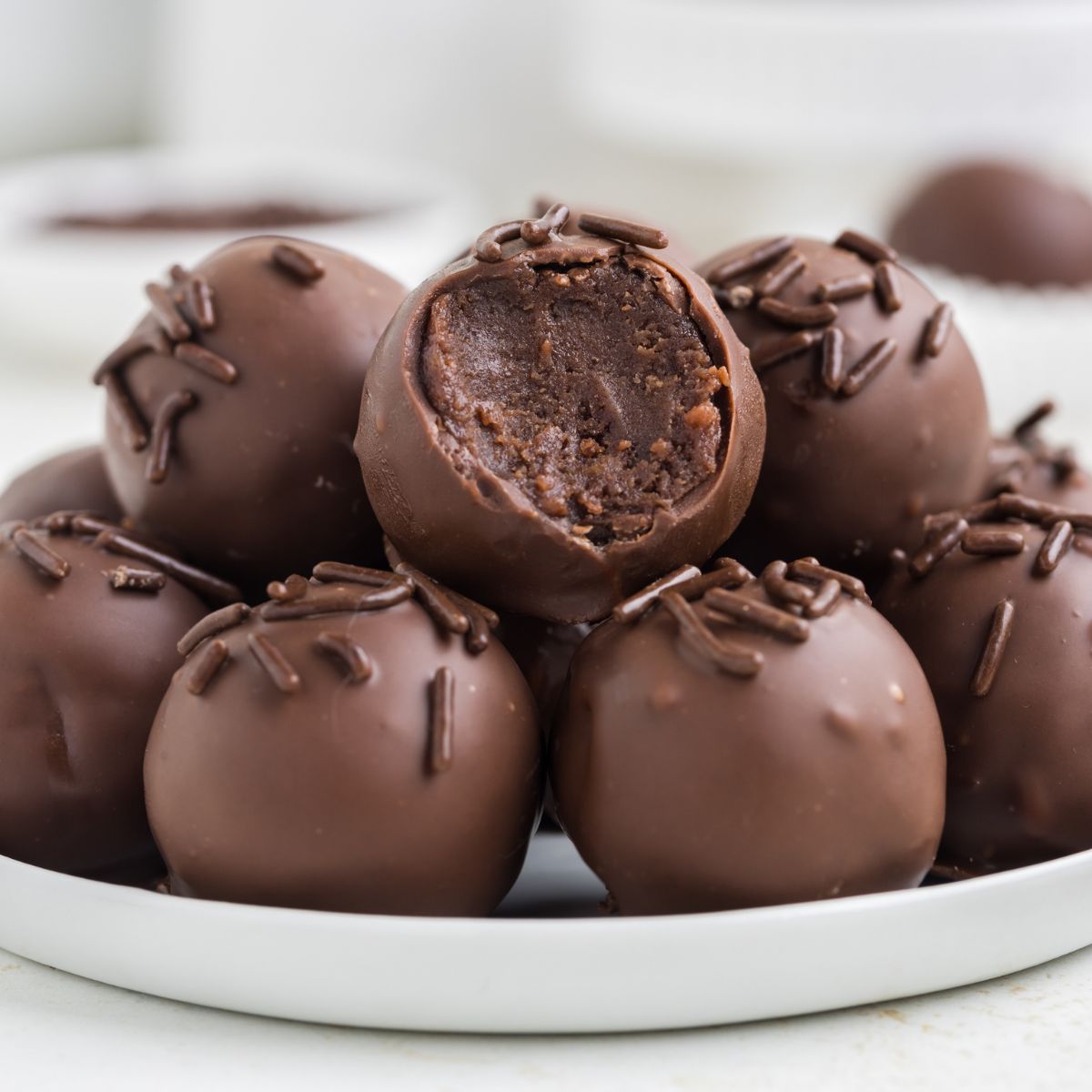 Brownie truffles piled on a plate with a bite missing from the top truffle.