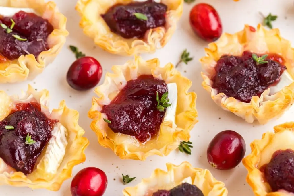 Brie and cranberry phyllo cups arranged on a plate surrounded by fresh cranberries.