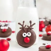 Cute fudge covered Oreo reindeer propped up against a bottle of milk.