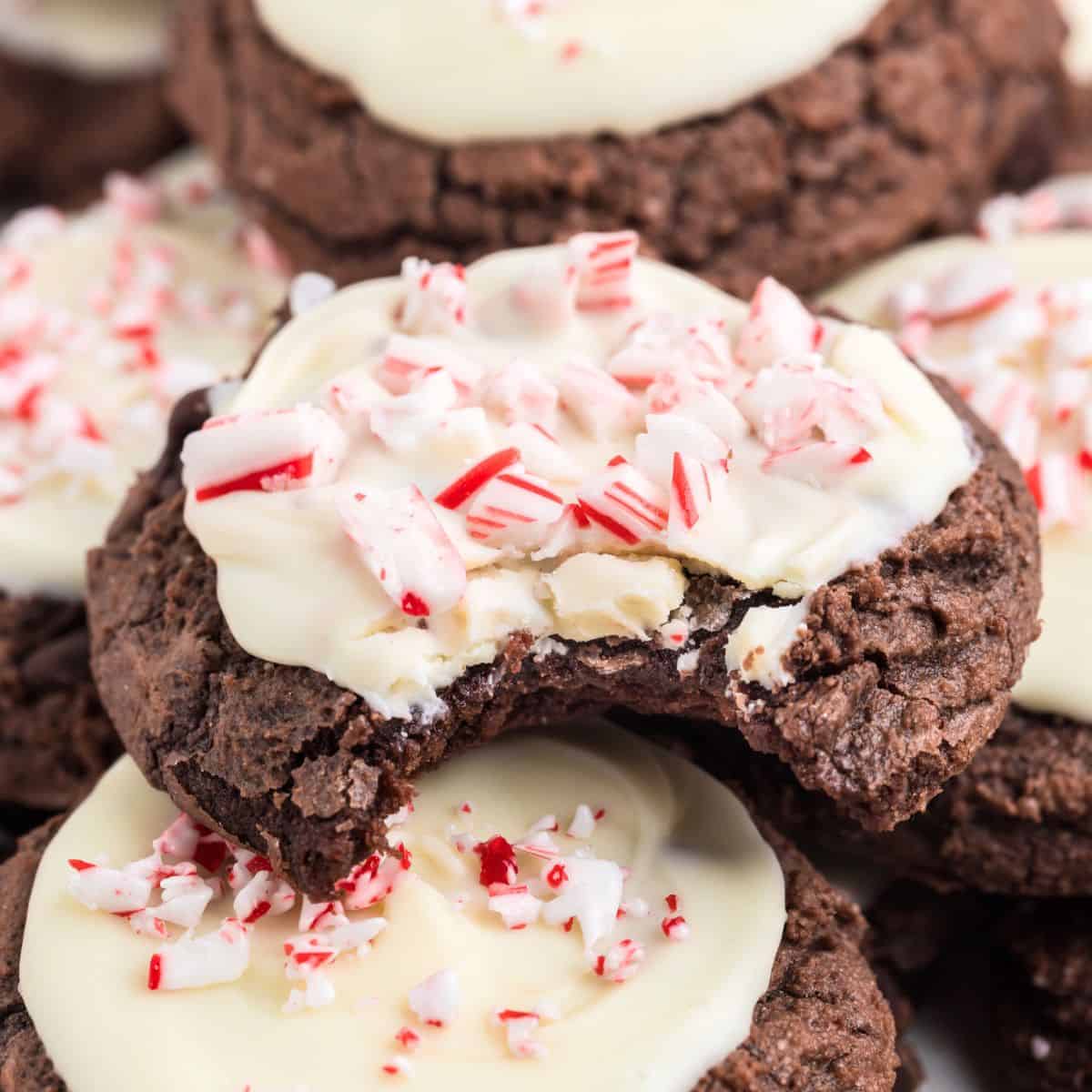 Peppermint Bark Brownie Cookies topped with white icing and crushed peppermint, one cookie partially eaten.