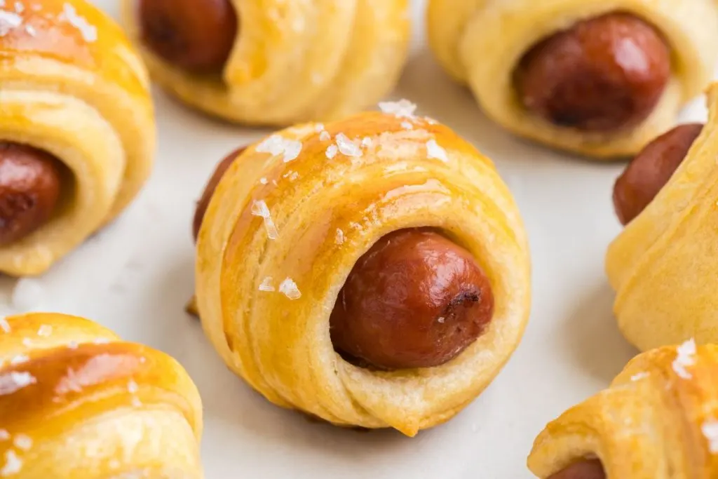 Crescent roll pigs in a blanket arranged on a parchment lined tray.
