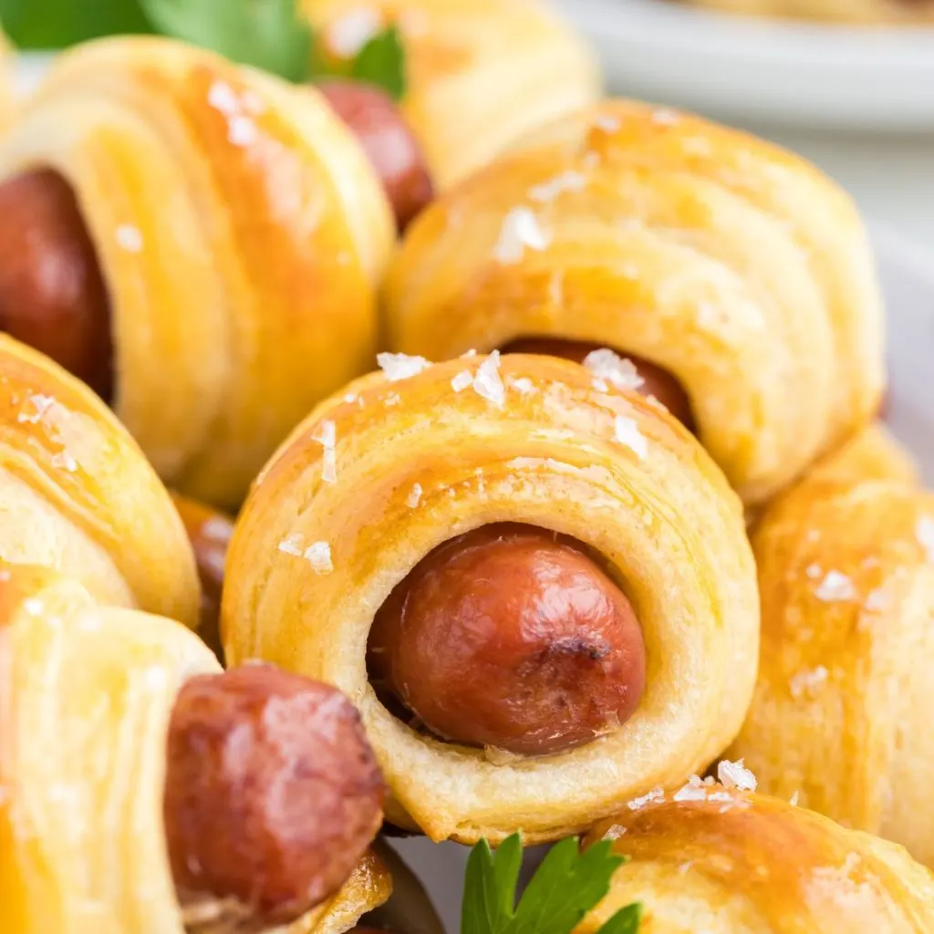 Pile of crescent roll pigs in a blanket with Italian parsley garnish.