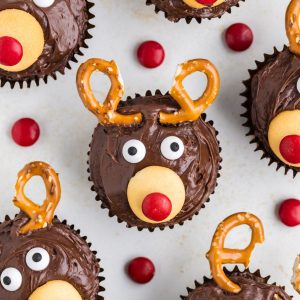 Six easy reindeer cupcakes arranged on the counter and surrounded by red M&Ms.