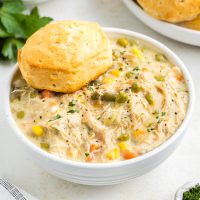 Bowl of slow cooker chicken pot pie topped with biscuits on the counter.
