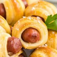 Pile of crescent roll pigs in a blanket with Italian parsley garnish.