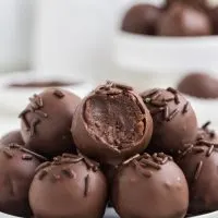 Brownie truffles piled on a plate with a bite missing from the top truffle.