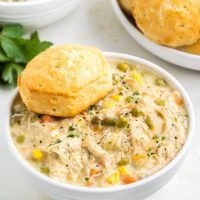 Two bowls on slow cooker chicken pot pie topped with biscuits on the counter.