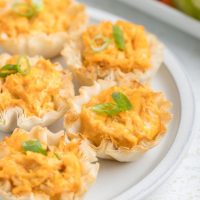 Buffalo chicken phyllo cups on a plate with carrots and celery in the background.