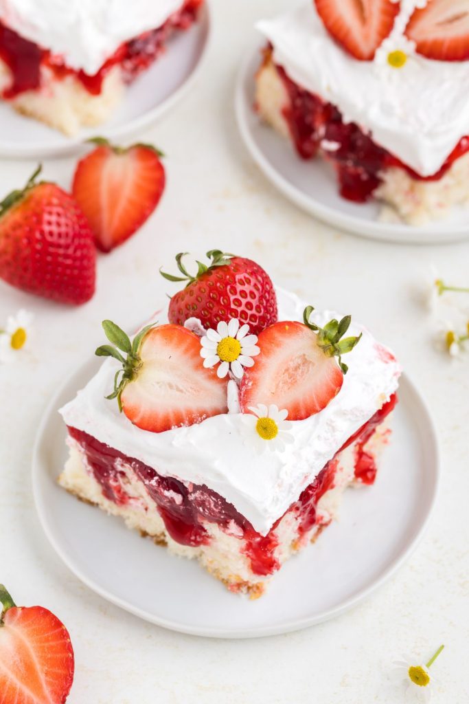 Slice of Strawberry Shortcake Poke Cake with fresh strawberries on a plate.