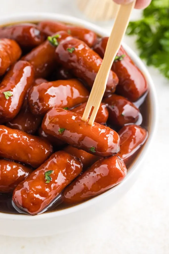 Bowl of grape jelly little smokies with a toothpick in one of the sausages. 