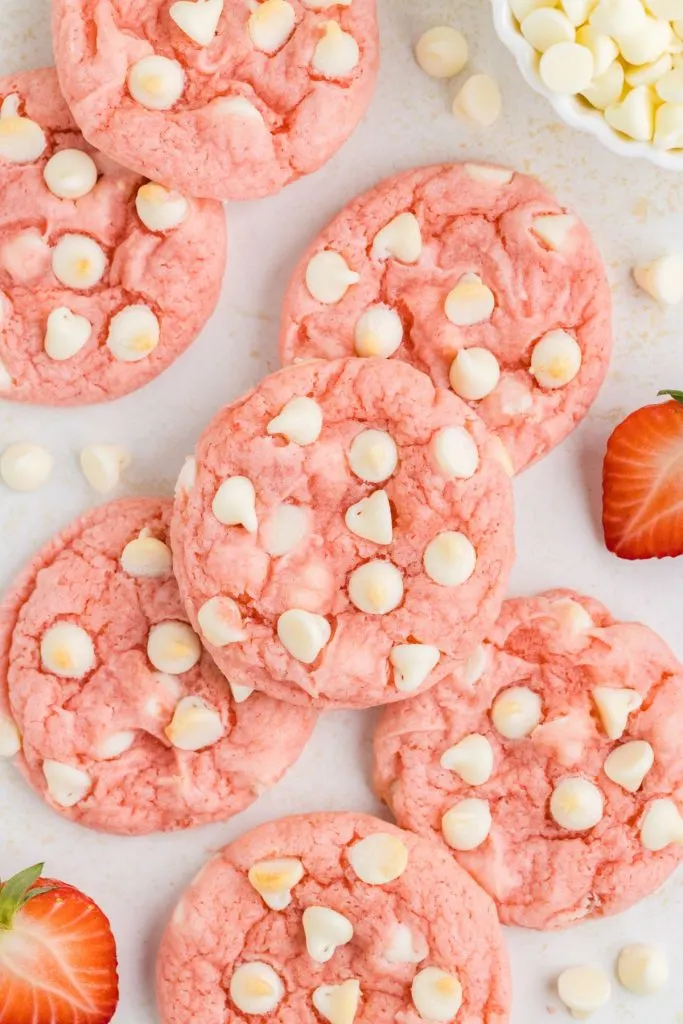 Strawberry white chocolate chip cookies arranged on the counter with a bowl of white chocolate chips. 
