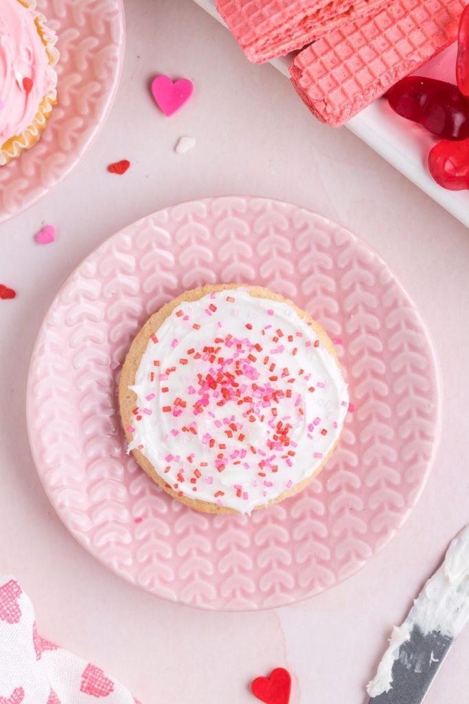 Sugar cookie frosted with white frosting and covered in pink sprinkles.