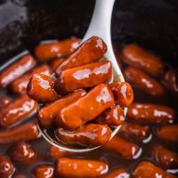 Spoonful of cocktail weenies being removed from the slow cooker.