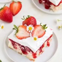 Slice of Strawberry Shortcake Poke Cake with fresh strawberries on a plate.