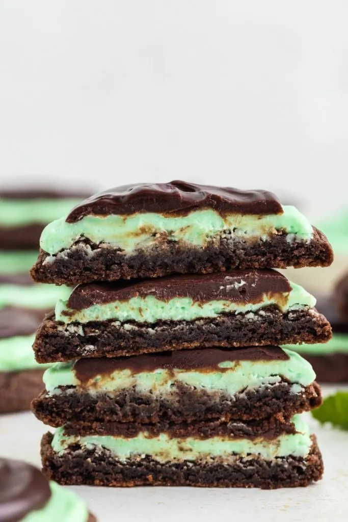 A stack of grasshopper cookies, cut in half, showcasing chocolate cookies and mint frosting.