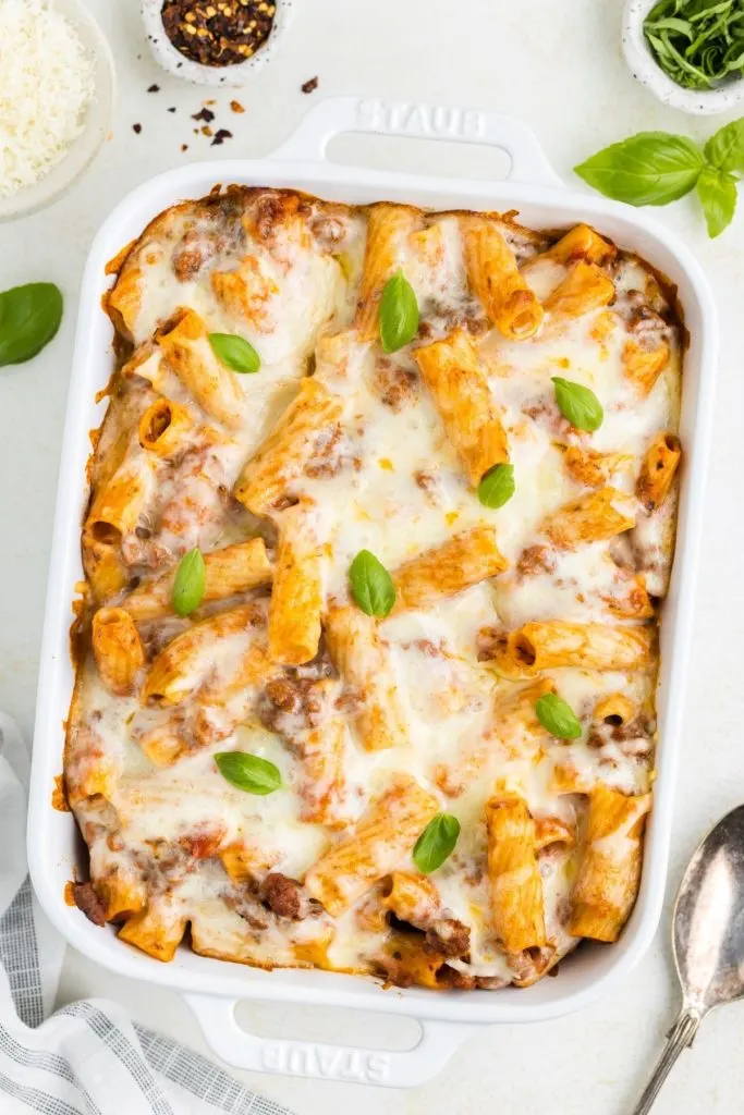 Cheesy beef pasta bake in a white casserole dish, garnished with fresh basil leaves.
