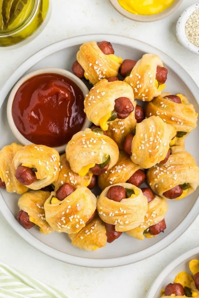 Plate full of pigs in a blanket with a ramekin of ketchup. 