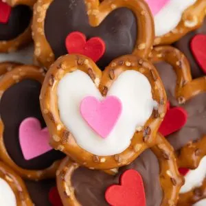 Pile of chocolate filled pretzels with heart sprinkles.
